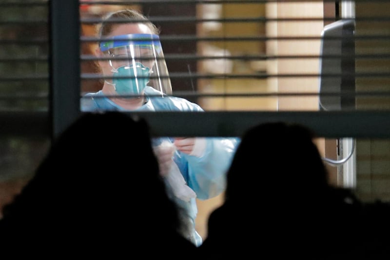 A worker wearing protective gear is seen through a window as she works in the room of Susan Hailey, 76, who has tested positive for the new coronavirus, as Hailey's daughters look in from outside the window, at the Life Care Center in Kirkland, Washington, near Seattle. AP Photo