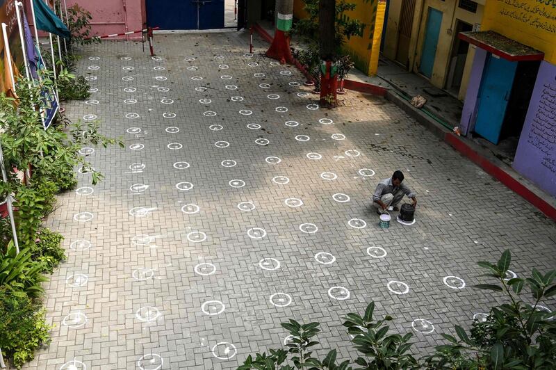 A worker draws markings on the ground for social distancing at a school in Lahore. AFP