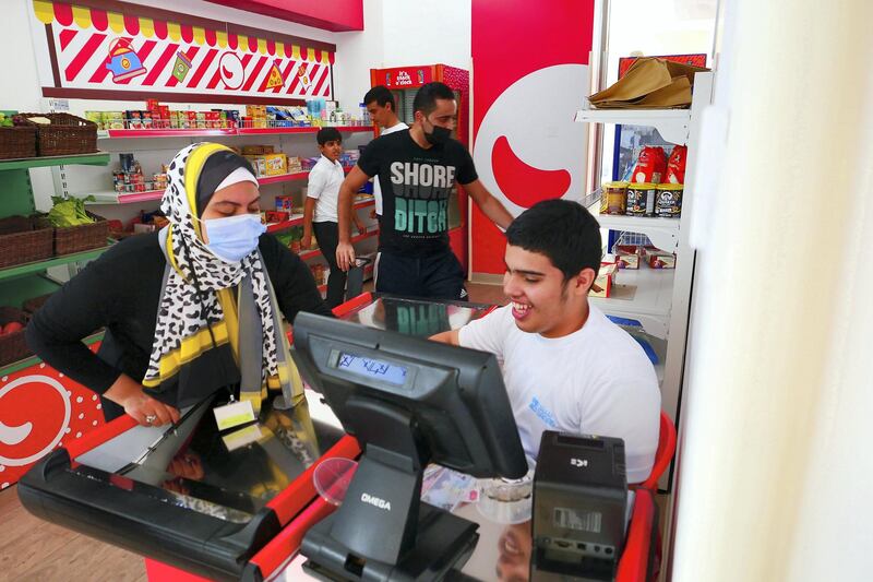 Omar Al Suwaidan (right) as a cashier at the Zoom market at the Sanad village mall in Dubai Sustainable City on April 29,2021. This centre is for people of determination fit out with real simulation zones like malls, clinics and an airport to help students gain independence. Pawan Singh / The National. Story by Kelly