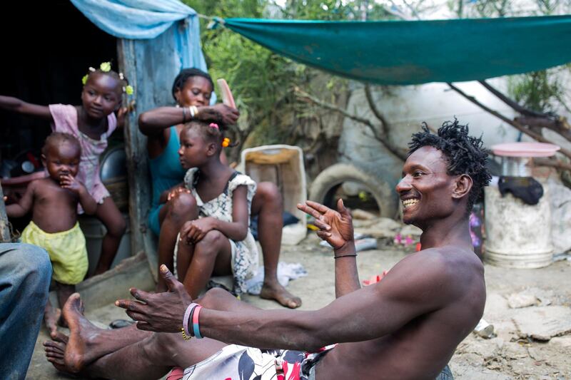 He jokes with a friend as his wife Violene Mareus braids their 9-year-old daughter Changline's hair outside their home near the Truitier landfill. AP Photo