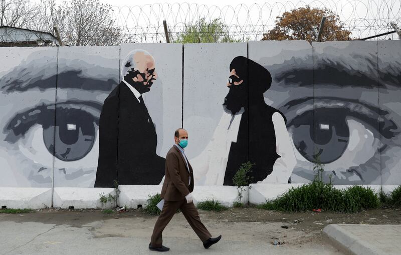 FILE PHOTO: An Afghan man wearing a protective face mask walks past a wall painted with photo of Zalmay Khalilzad, U.S. envoy for peace in Afghanistan, and Mullah Abdul Ghani Baradar, the leader of the Taliban delegation, in Kabul, Afghanistan April 13, 2020.REUTERS/Mohammad Ismail/File Photo