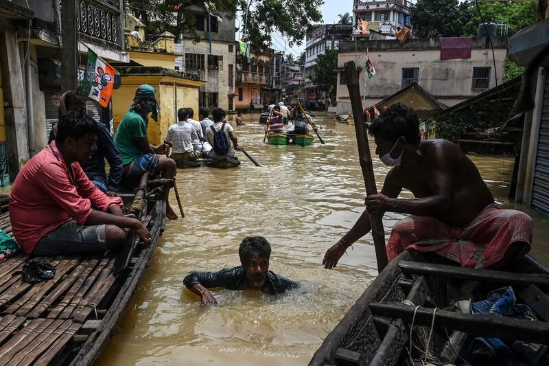 A man sitting on a boat helps a man to navigate his way through floodwaters in Ghatal, Paschim Medinipur district, India.