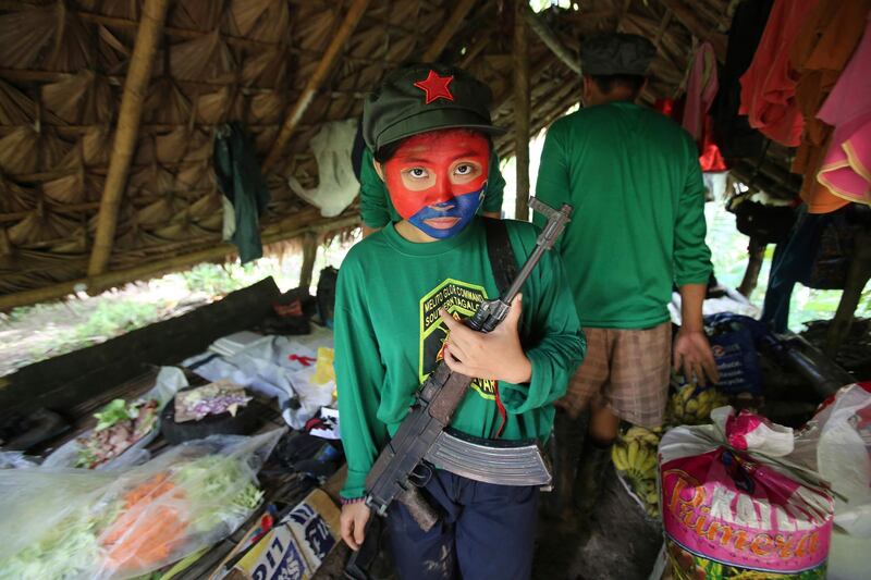FILE - In this Nov. 23, 2016 photo, a woman New People's Army guerrilla with her face painted to conceal her identity holds her firearm inside a shelter at a rebel encampment tucked in the harsh wilderness of the Sierra Madre mountains, southeast of Manila, Philippines. Communist guerrillas are marking half a century of their rural rebellion in the Philippines with threats of more attacks, possibly spreading into cities, as a negotiated settlement remained elusive with peace talks repeatedly stalling. (AP Photo/Aaron Favila, File)