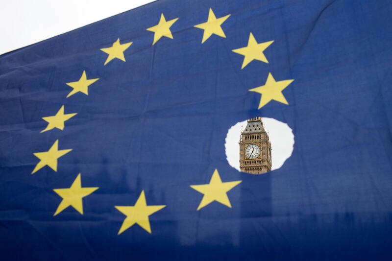(FILES) In this file photo taken on March 29, 2017 a pro-remain protester holds up an EU flag with one of the stars symbolically cut out, in front of the Houses of Parliament shortly after British Prime Minister Theresa May announced to the House of Commons that Article 50 had been triggered in London.  A bill enacting Britain's decision to leave the European Union has become law after months of debate, the speaker of parliament announced on June 26, 2018, to cheers from Conservative Party lawmakers. / AFP / OLI SCARFF

