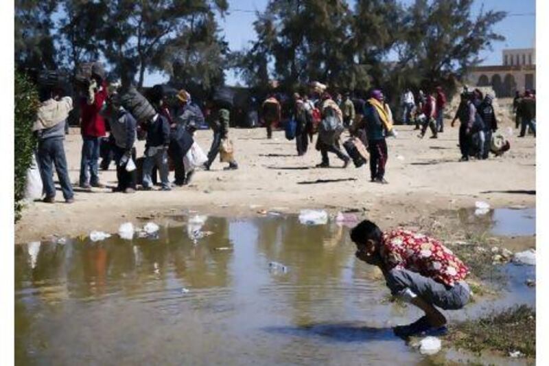 A migrant worker from Bangladesh washes off in a puddle at the Ras Ajdir border checkpoint yesterday in Libya.