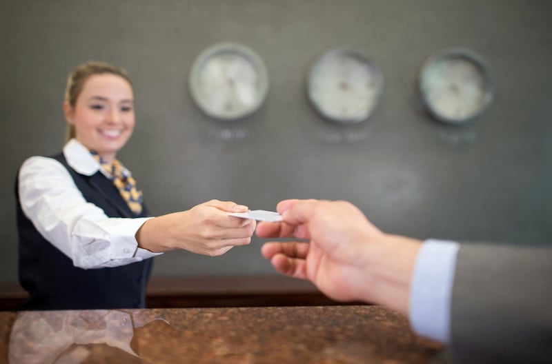 Woman working at a hotel handing a loyalty card or card key at the front desk