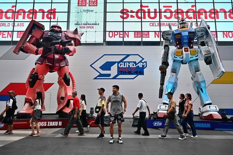 A man poses for a picture in between two giant Gundam statues by Bandai Namco in front of Central World shopping mall in Bangkok. AFP