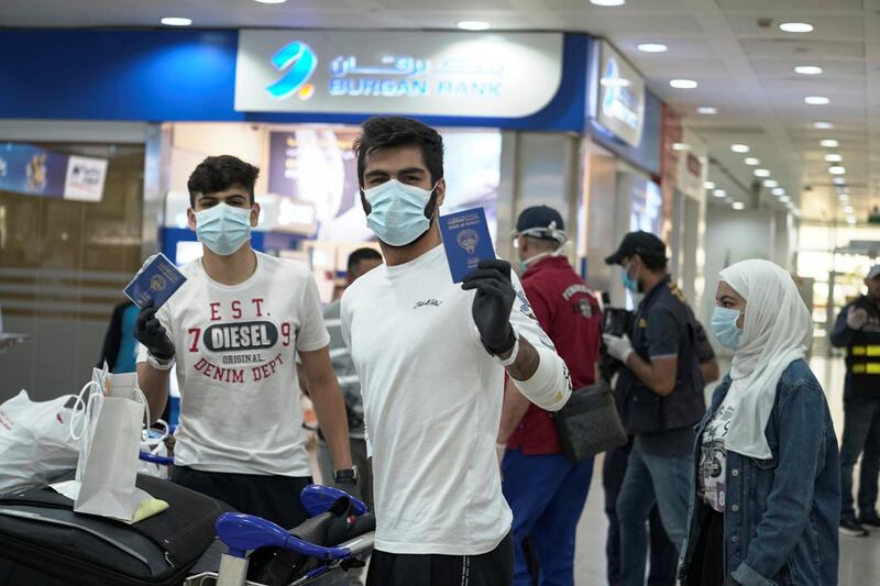 Kuwaiti boys wearing protective face masks and quarantine tracking bracelets, following the outbreak of the coronavirus disease (COVID-19), pose for the camera as they hold up their passports upon arrival from Amman, to Kuwait Airport in Kuwait, Kuwait April 21, 2020. REUTERS