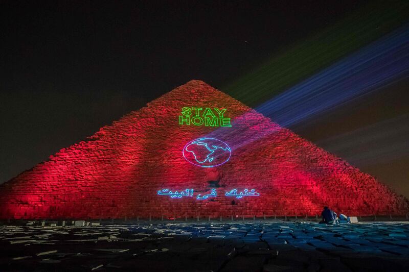A man takes pictures in front of the Great pyramid of Kheops where a laser projection writes "Stay home" on March 30, 2020. AFP