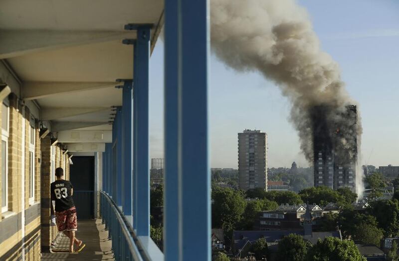 A resident in a nearby building watches smoke rising from Grenfell Tower, where 58 people died in a fire.  Matt Dunham / AP 