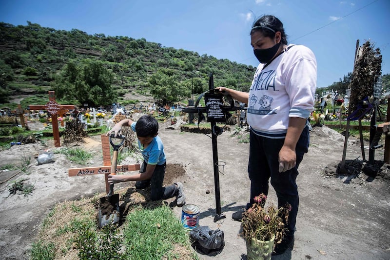 A woman visits two family members who died of COVID-19 while a 10-year-old boy works placing crosses at the San Miguel Xico cemetery on August 5, 2020. AFP