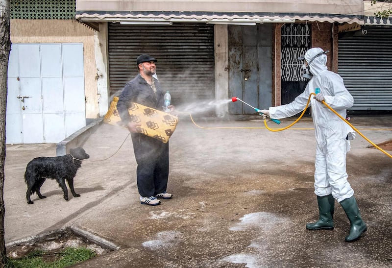TOPSHOT - A Moroccan health ministry worker disinfects a man walking a dog and carrying a mat in the capital Rabat on March 22, 2020. A public health state of emergency went into effect in the Muslim-majority country late on March 20, and security forces and the army have been deployed on the streets to combat the spread of COVID-19 coronavirus disease. People have been ordered to stay at home, and restrictions on public transport and travel between cities are also in place. / AFP / FADEL SENNA
