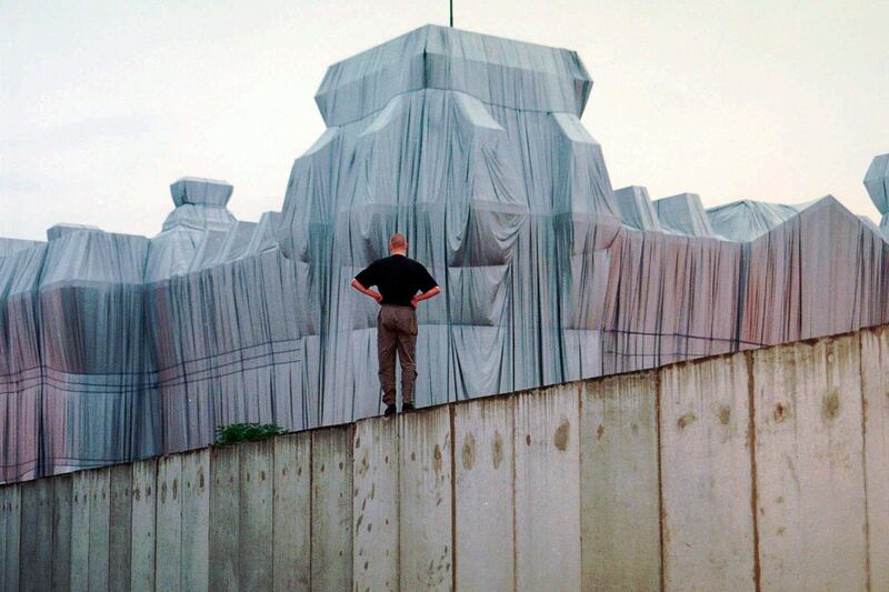 In this June 22, 1995, photo, a man stands at the top of the remains of the Berlin Wall and looks at the wrapped Reichstag building, a project titled 'Wrapped Reichstag' by artist Christo and his wife Jeanne-Claude. AP