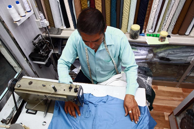 A tailor makes a dishdasha in Oman. The influx of shorter hemlines, elaborate embroidery and multicoloured designs has been blamed on foreign imports.