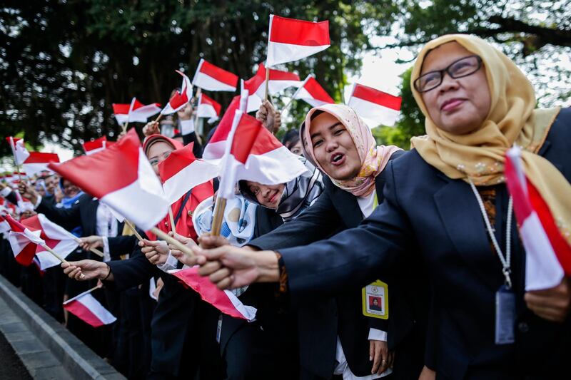 Indonesian presidential palace staff wave national flags as Indonesian President Joko Widodo leaves Merdeka palace for parliament building to be sworn in for his second five-year term.  EPA