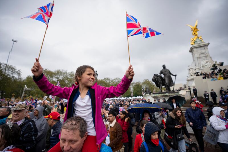 A girl waves Union Jack flags as King Charles and Queen Camilla wave to the crowds from the balcony of Buckingham Palace. AP