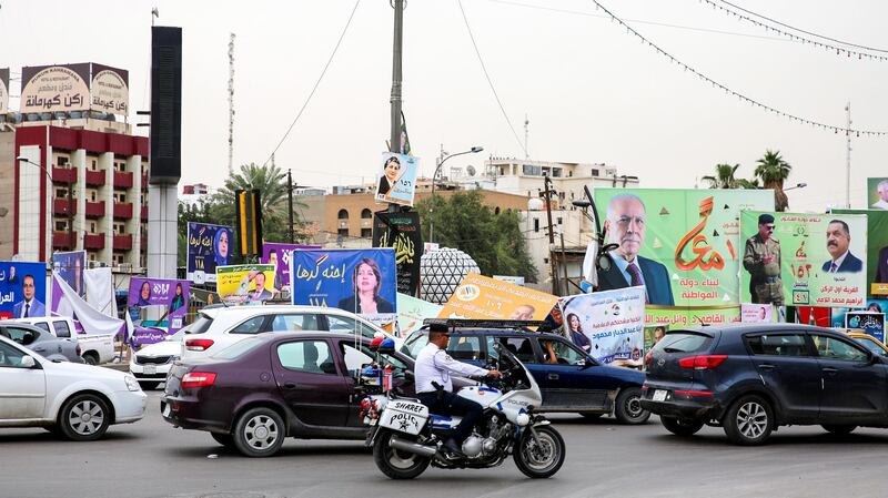 An Iraqi policeman rides a motorcycle amdist traffic past electoral banners for candidates in the upcoming parliamentary polls that were damaged by a storm the day before, in the capital Baghdad on April 28, 2018.  / AFP PHOTO / SABAH ARAR