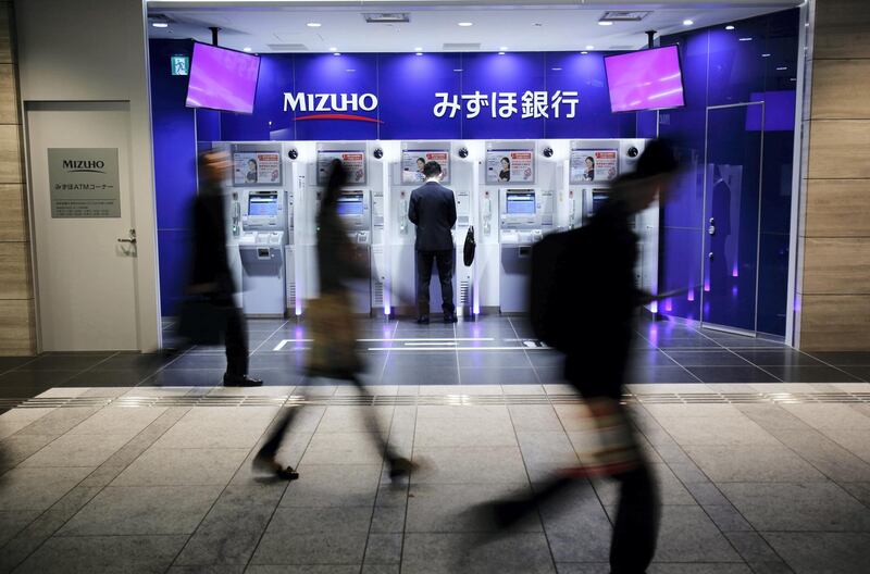 A man uses an ATM machine of Mizuho Bank as pedestrians walk past at a train station in Tokyo November 13, 2013. Japan's Mizuho Financial Group said net profit jumped 133.2 percent in the first half of its financial year compared with a year ago, driven by a rally in stocks that boosted the value of its equity portfolio. Picture taken November 13, 2013. REUTERS/Yuya Shino (JAPAN - Tags: BUSINESS) - GM1E9BE15ZM01