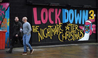 Pedestrians walk past graffiti reading "Lockdown 3: The Nightmare after Christmas" painted on a boarded up restaurant passes a Government Covid-19 information poster near a road in Manchester, northern England, on February 15, 2021. Britain intends to seek a "cautious but irreversible" ending of strict coronavirus restrictions, Prime Minister Boris Johnson said Monday as his government introduced hotel quarantine stays for arrivals from "high risk" nations. / AFP / Oli SCARFF
