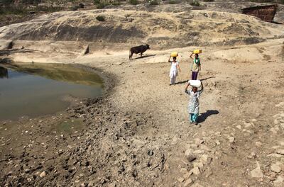 Women carry containers to collect drinking water from an almost dried up well at Talad village near Jammu. AP