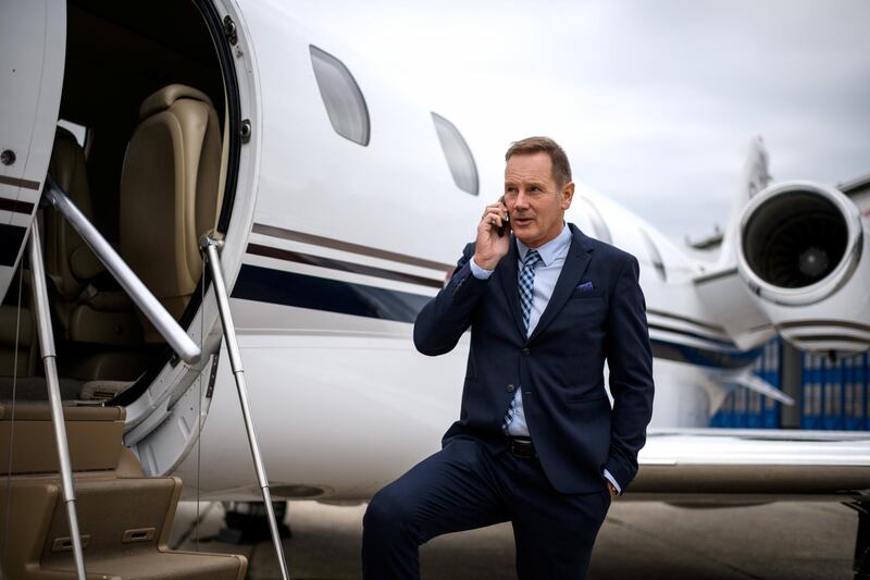 Senior man wearing elegant clothes standing next to private jet airplane and talking over mobile phone.
