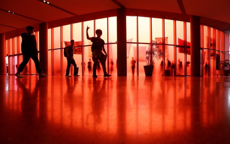 One student leads others to an exit past the translucent red walls of Seattle City Hall, where other student climate activists are seen protesting outside during a climate strike.  AP Photo