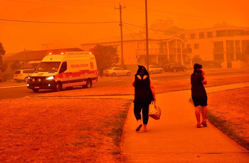 A Fire and Rescue NSW Rehabilitation vehicle drives past people walking along a road shrouded in smoke in Batemans Bay, New South Wales, Australia. Bloomberg