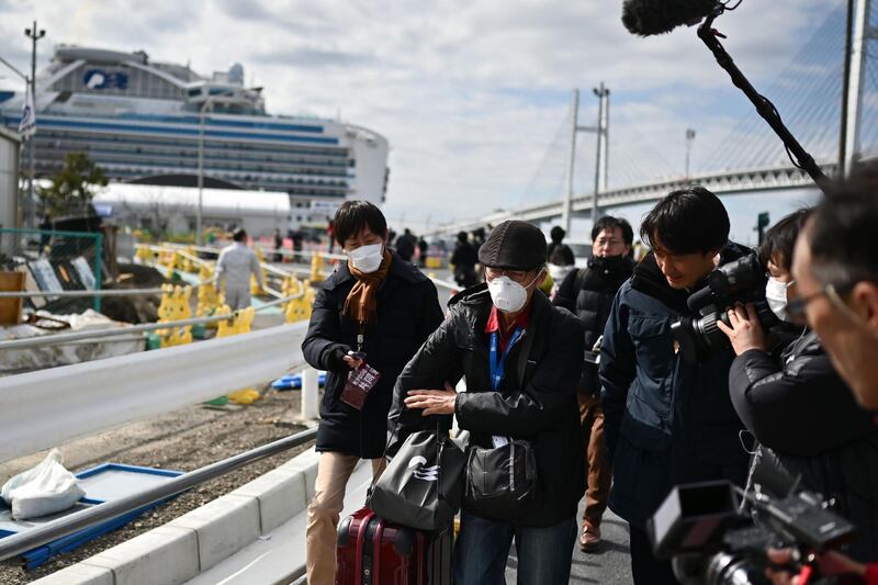 A passenger (C) leaves on foot after dismembarking the Diamond Princess cruise ship (back, L) in quarantine due to fears of the new COVID-19 coronavirus, at the Daikoku Pier Cruise Terminal in Yokohama.  AFP