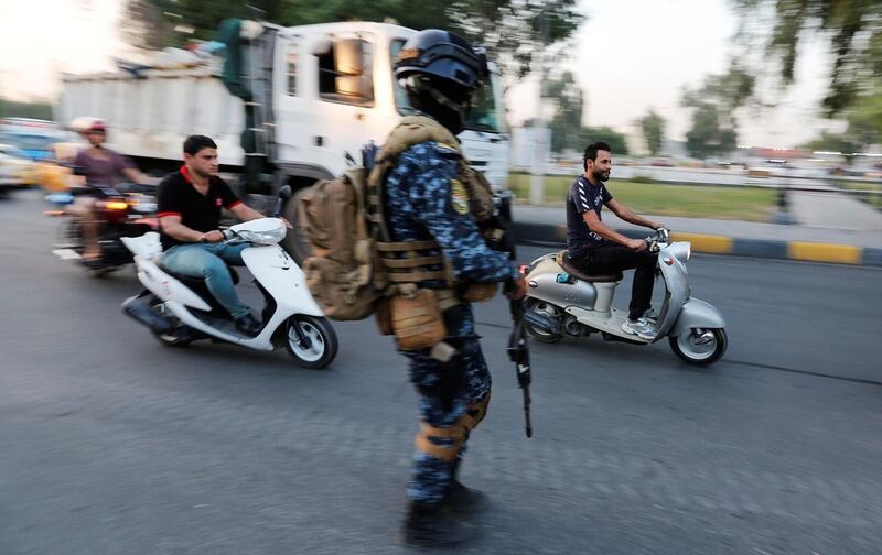 Men ride motorbikes past a member of Iraqi federal police in a street in Baghdad, Iraq. REUTERS