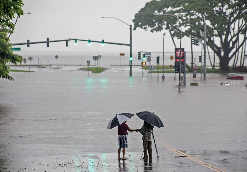 People stand near flood waters  in Hilo, Hawaii. Hollyn Johnson / Hawaii Tribune-Herald via AP