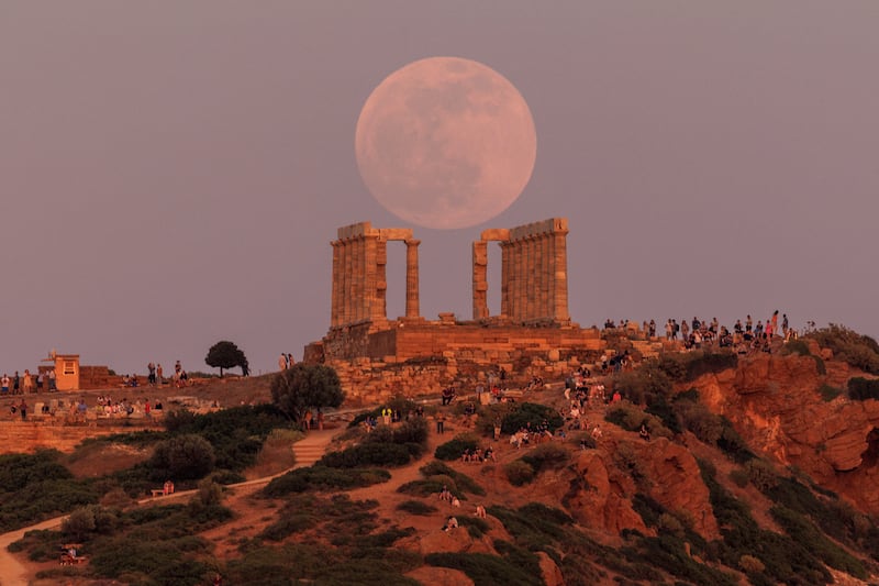 People watch a full moon, known as the "Flower Moon", rising behind the Temple of Poseidon, before a lunar eclipse in Cape Sounion, near Athens, Greece, May 15, 2022.  REUTERS / Alkis Konstantinidis