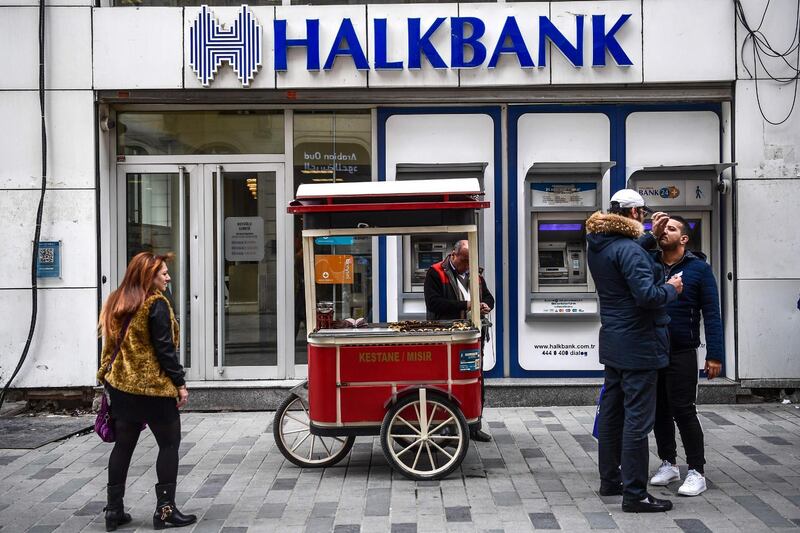(FILES) In this file photo taken on December 1, 2017, people walk by as a street vendor stands in front of a branch of the Turkish bank Halkbank on in Istanbul.  US federal prosecutors filed criminal charges against Turkey's state-run Halkbank on October 15, 2019, for allegedly participating in a multi-billion-dollar scheme to evade economic sanctions on Iran. The Department of Justice said it had charged the bank with six counts of fraud, money laundering, and sanctions offenses. "This is one of the most serious Iran sanctions violations we have seen," Assistant Attorney General John Demers said in a statement announcing the indictment / AFP / OZAN KOSE
