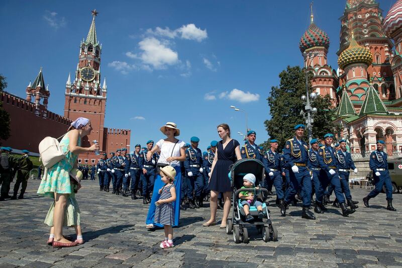 Women walk with their children as Russian paratroopers marsh during celebrations of Paratroopers Day in Red square in Moscow, Russia, Thursday, Aug 2, 2018, with St.Basil Cathedral, right, and Kremlin's Spasskaya tower, left, in the background. Paratroopers are an elite unit of the Russian Army, and everyone in the country recognizes their blue berets. (AP Photo/Pavel Golovkin)
