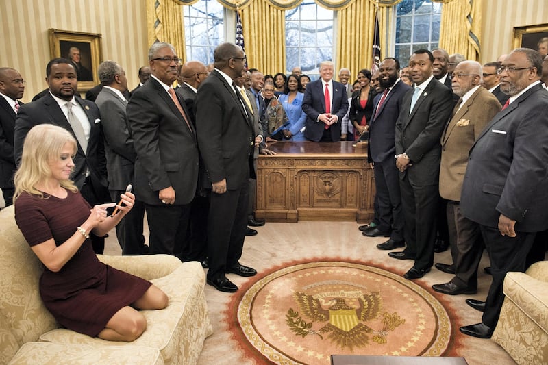 Counselor to the President Kellyanne Conway (L) checks her phone after taking a photo as US President Donald Trump and leaders of historically black universities and colleges pose for a group photo in the Oval Office of the White House before a meeting with US Vice President Mike Pence February 27, 2017 in Washington, DC. (Photo by Brendan Smialowski / AFP)