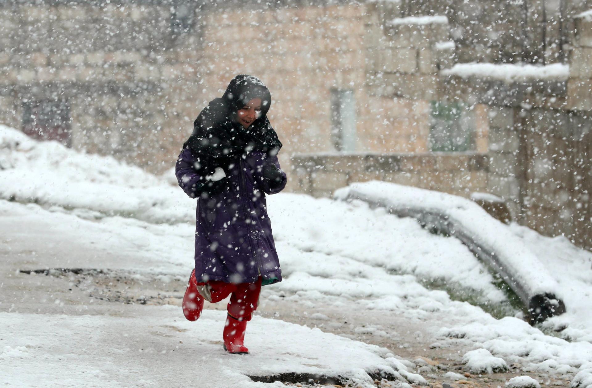 A young Syrian girl runs on a snow-covered street in the Jabal Al Zawiya region in the rebel-held northern countryside of Syria's Idlib province, on February 17, 2021.   AFP