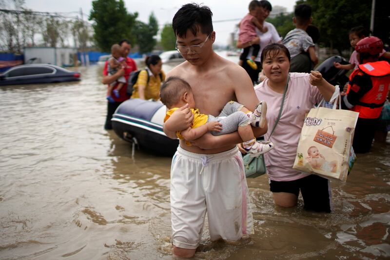 A man holding a baby wades through a flooded road following heavy rainfall in Zhengzhou, Henan province, China.