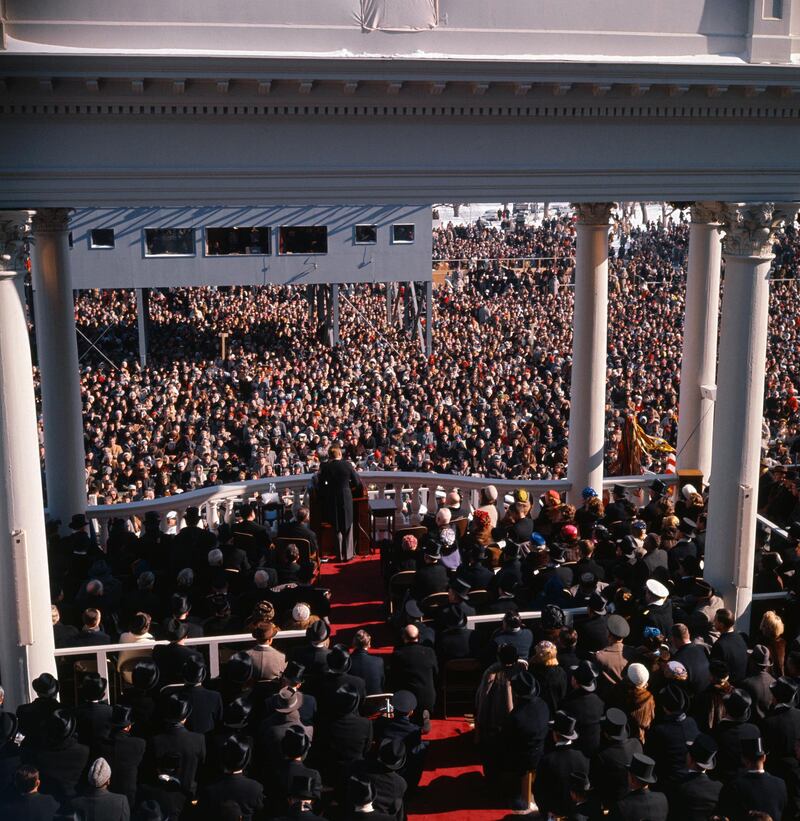 Back view of President John F. Kennedy and crowd as he gives inaugural speech.