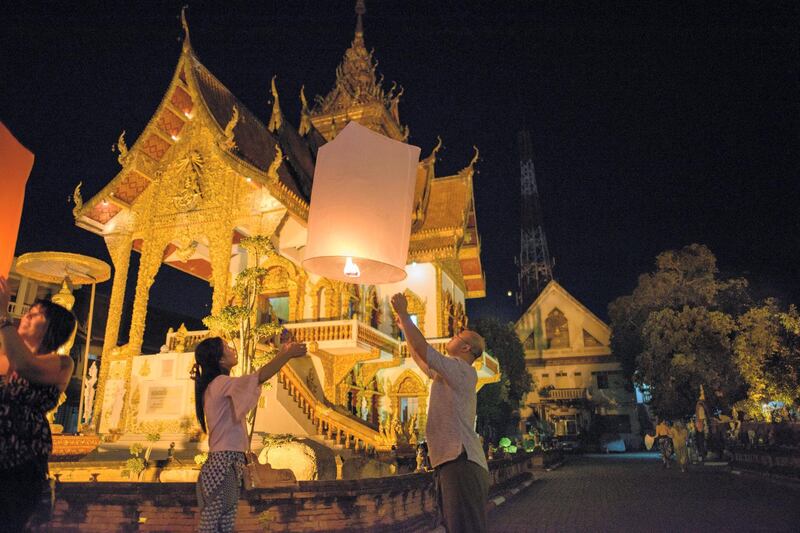 In this photograph taken on November 4, 2017, a man and a woman release a lit lantern at a local buddhist temple as they celebrate during the Loy Krathong festival in Chiang Mai. - Chiang Mai is considered as one of the best places to experience the Loy Krathong festival in Thailand which is celebrated on the first full moon of the 12th traditional Thai calendar and which includes a theme float parade through town. Thousands of people that included tourists and locals alike lined the streets to watch the display of elaborate floats. (Photo by Roberto SCHMIDT / AFP)