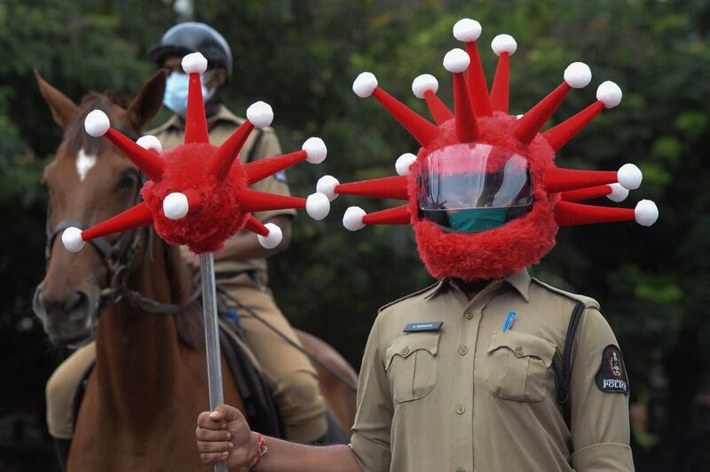 Police personnel wearing a Covid-19 coronavirus-themed helmets and battons stand in formation as they take part in awareness campaign against the pandemic at a traffic junction in Hyderabad on June 9, 2021. / AFP / NOAH SEELAM
