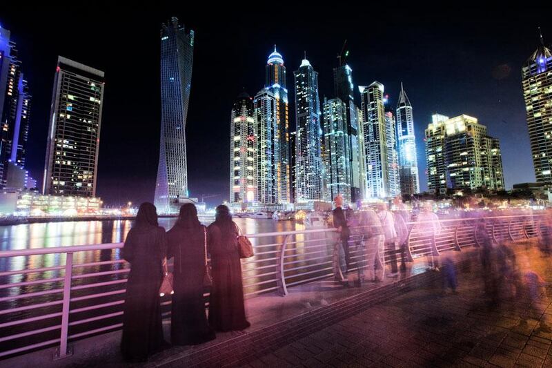 Groups of people come and go to admire the colourful skyline of the Dubai marina at night.  Jaime Puebla / The National