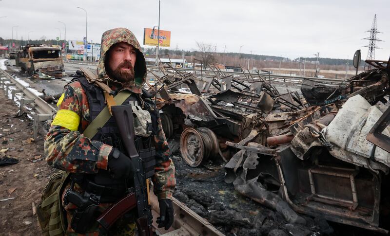 An armed man stands by the remains of a Russian military vehicle in Bucha, close to the capital Kyiv, Ukraine, Tuesday, March 1, 2022.  Russia on Tuesday stepped up shelling of Kharkiv, Ukraine's second-largest city, pounding civilian targets there.  Casualties mounted and reports emerged that more than 70 Ukrainian soldiers were killed after Russian artillery recently hit a military base in Okhtyrka, a city between Kharkiv and Kyiv, the capital.  (AP Photo / Serhii Nuzhnenko)