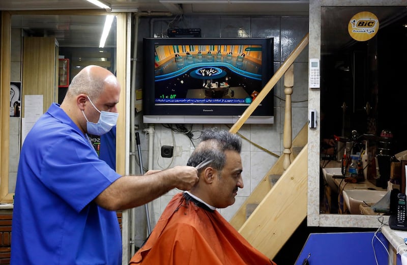 An Iranian hairdresser works as the first presidential candidates' TV debate shows presidential candidate Ebrahim Raisi speaking. EPA
