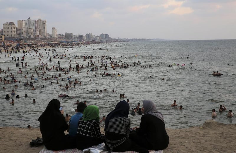 A Palestinian family talk while large crowds of people swim at the Gaza City beach. Adel Hana / AP Photo