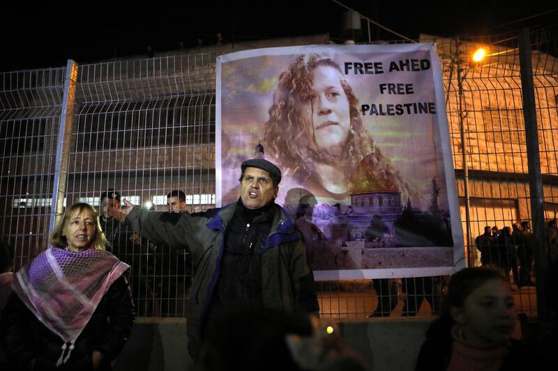 epa06486483 Palestinian and International activists stand near a picture of Ahed Tamimi during a protest in solidarity with Ahed Tamimi, near the Ibrahimi mosque, also known as Cave of Patriarchs, in the West Bank city of Hebron, 30 January 2018. Palestinian celebrate the birthday of Ahed Tamimi near an Israeli fence, 17 years old Ahd was arrested after assaulting Israeli soldiers who break into her house during clashes near Ramallah.  EPA/ABED AL HASHLAMOUN