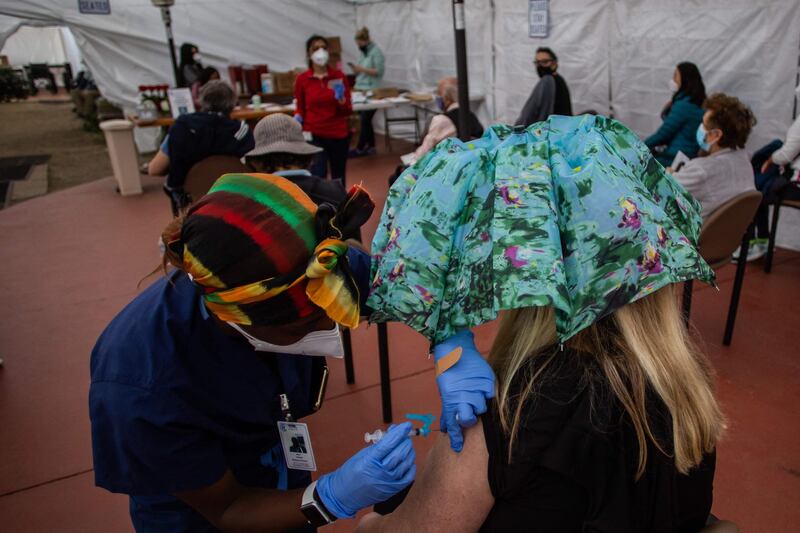 Registered Nurse Myra Braziel administers a Moderna Covid-19 vaccine to a woman using an umbrella to keep social distance, at Kedren Community Health Center, in South Central Los Angeles, California. AFP