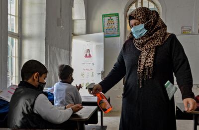 A member of staff disinfects the hands pupils as they attend class on the first day of the new academic year the northern city of Mosul, on November 29, 2020, amid the COVID-19 pandemic. Iraq's schools began a new academic year, after weeks of delay due to the coronavirus pandemic. Children will attend class in person once a week on rotating shifts, and will take online (distant learning) courses the rest of the week. / AFP / Zaid AL-OBEIDI
