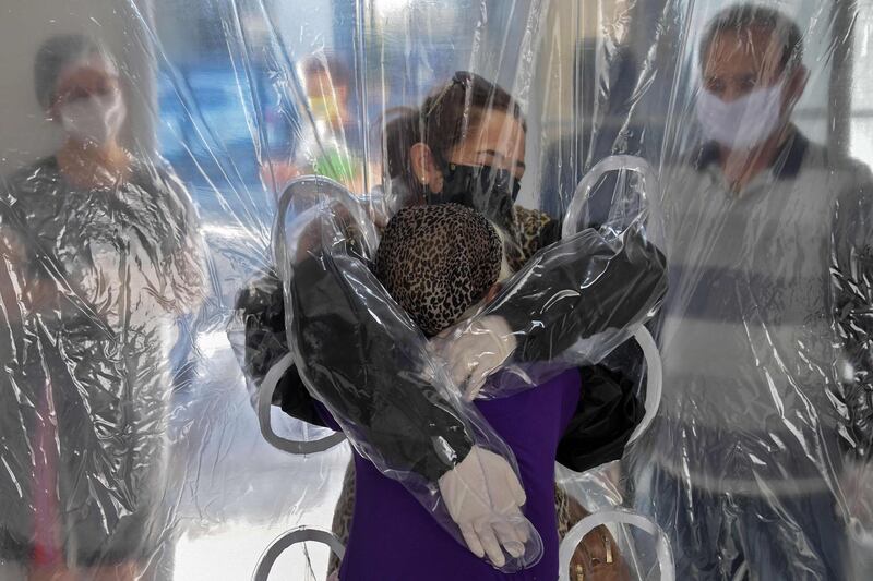 Elisabete Nagata (top) hugs her 76-year-old sister-in-law Luiza Nagata, through a transparent plastic curtain at a senior nursing home in Sao Paulo, Brazil amid the pandemic.  AFP