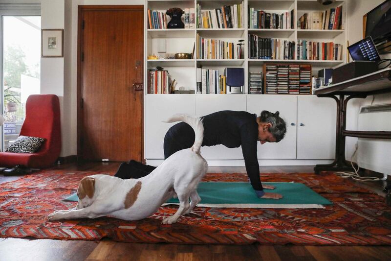 This picture taken on March 23, 2020 shows a woman taking part in an online pilates class at home, as her dog Elvis stretches next to her, in Nicosia, as restrictions on movement and social distancing were imposed across Cyprus to contain the spread of the COVID-19 novel coronavirus. / AFP / Christina ASSI
