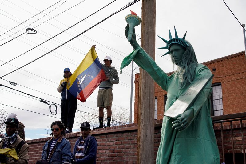 Venezuelan migrants hold their country's flag next to a replica of the Statue of Liberty. Reuters