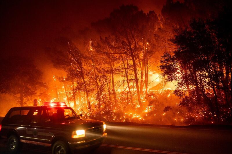 A fire vehicle passes burning trees on Pleasants Valley Rd. near Winters, California. AP